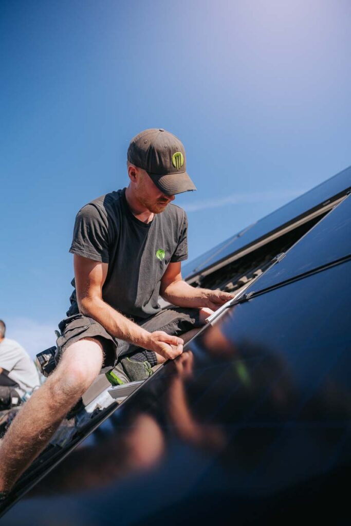 Mitarbeiter von PV Green steht auf Dach und rückt ein PV Modul zurecht.